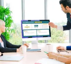 Business people meet around a computer monitor displaying a Customer Reviews dashboard