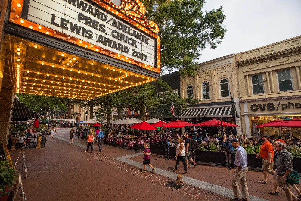 Downtown-mall- A bustling street scene with outdoor diners under red umbrellas, bright marquee lights, and shops lining the vibrant sidewalk.