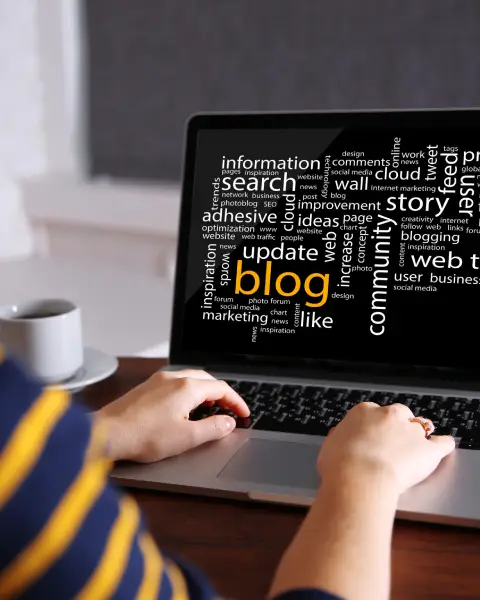 Hands type on a laptop displaying a word cloud with "blog," "story," "update," and "search" prominently featured